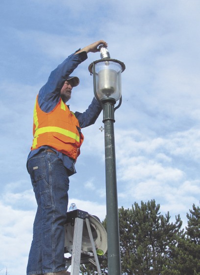 Sequim Public Works crew member Del Singer installs an LED unit in a sidewalk illuminating street lamp.