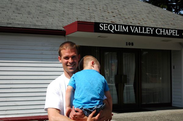 Danny Wakefield stands outside his new business while holding his napping 3-year-old-son. Wakefield lives locally with his family and recently partnered with his half-brother to buy the Sequim Valley Funeral Home from Dignity Memorial.