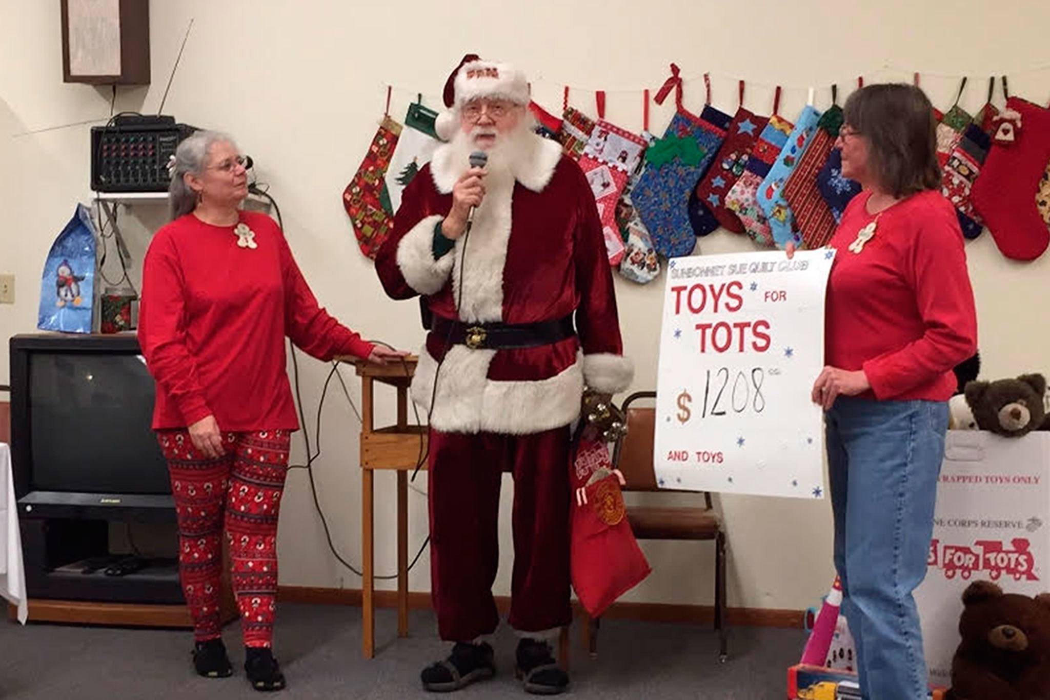 Sunbonnet Sue Quilt Club members Sharon Clayton and Marilyn Williams present Santa Claus with Clallam County Toys for Tots $1,208 in donations. Photo courtesy of Sharon Clayton