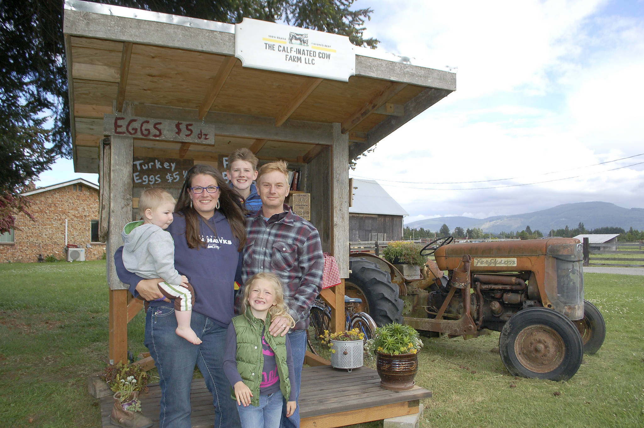 The Calf-inated Cow farm stand is one of the many in Sequim that offers fresh, local produce to passerby on a weekly basis. The farm’s owner Kristin Higgins, left, with youngest son Ivan, 1, William, 12, back center, husband Brian Higgins, right, and daughter Jane, 5, stand in front of their farm stand at 343 McComb Road. Sequim Gazette photo by Erin Hawkins