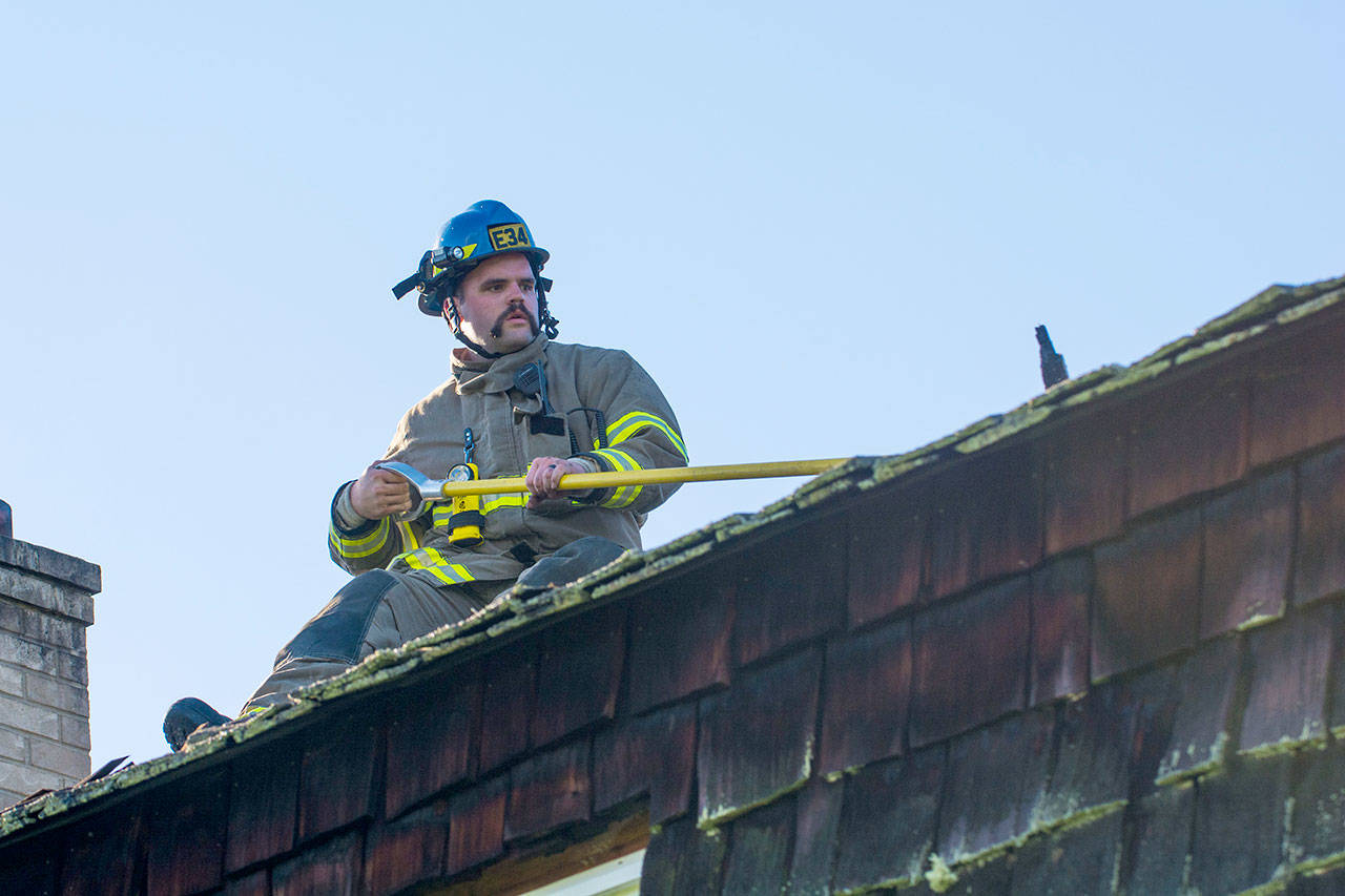 Clallam County Fire District No. 3 Firefighter Bryce Miginley overhauls a section of roof that caught fire near Sequim on Sunday. (Jesse Major/Olympic Peninsula News Group)