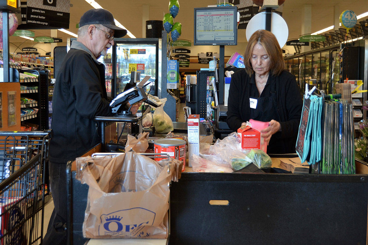 Kathy Johnson, a checker at Sequim QFC, helps Jack Guinn purchase his groceries on March 18. Starting April 1, QFC will no longer offer plastic bags at checkout stands to customers. Guinn said he’s been in the habit of using reusable bags since his former home of Shoreline banned the bags. Currently, no ban is proposed in Sequim. Sequim Gazette photo by Matthew Nash