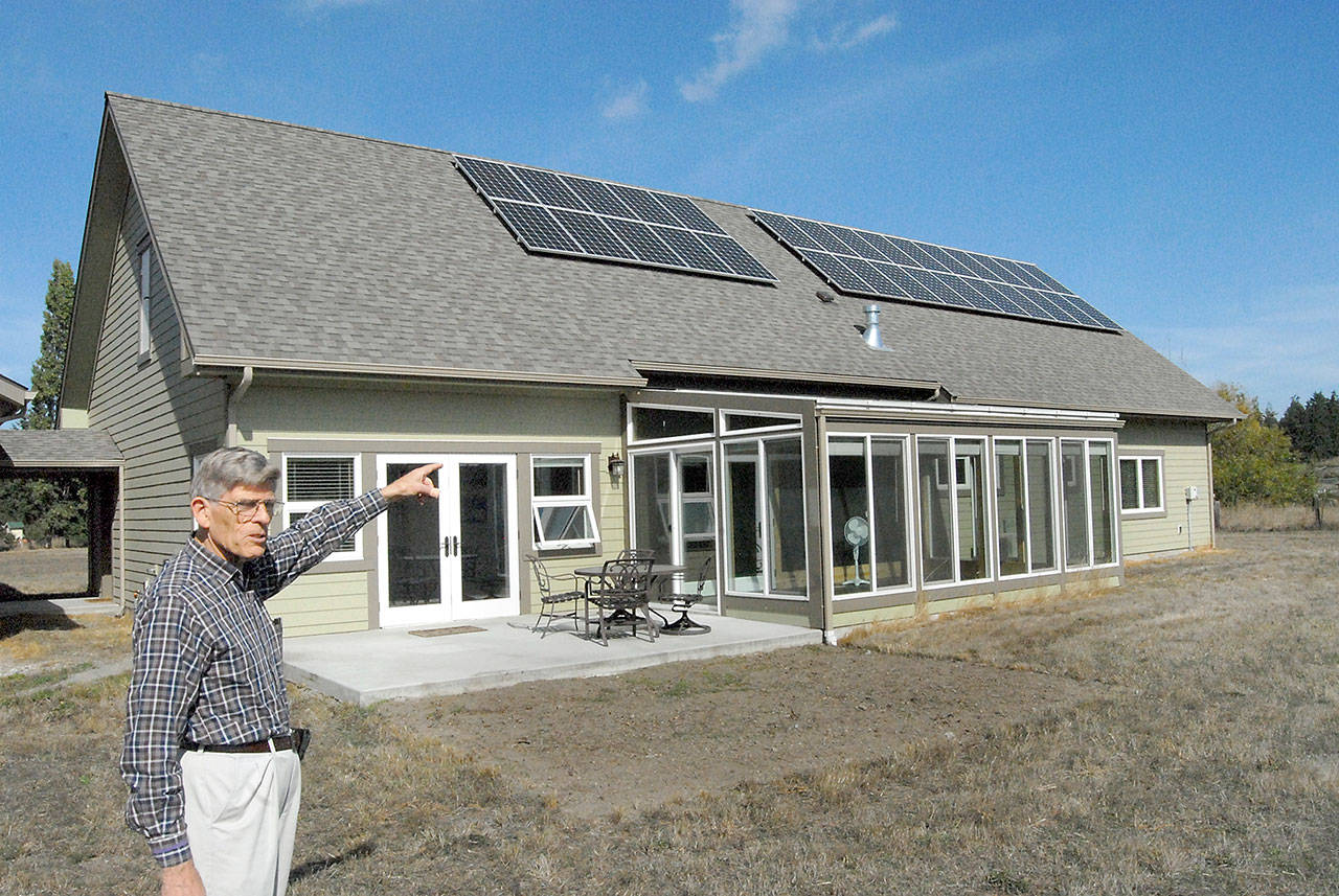 David Large points to a solar panel array and a glass-enclosed sun room that provide electricity and heat to his energy efficient home in rural Sequim in 2018. File photo by Keith Thorpe/Peninsula Daily News