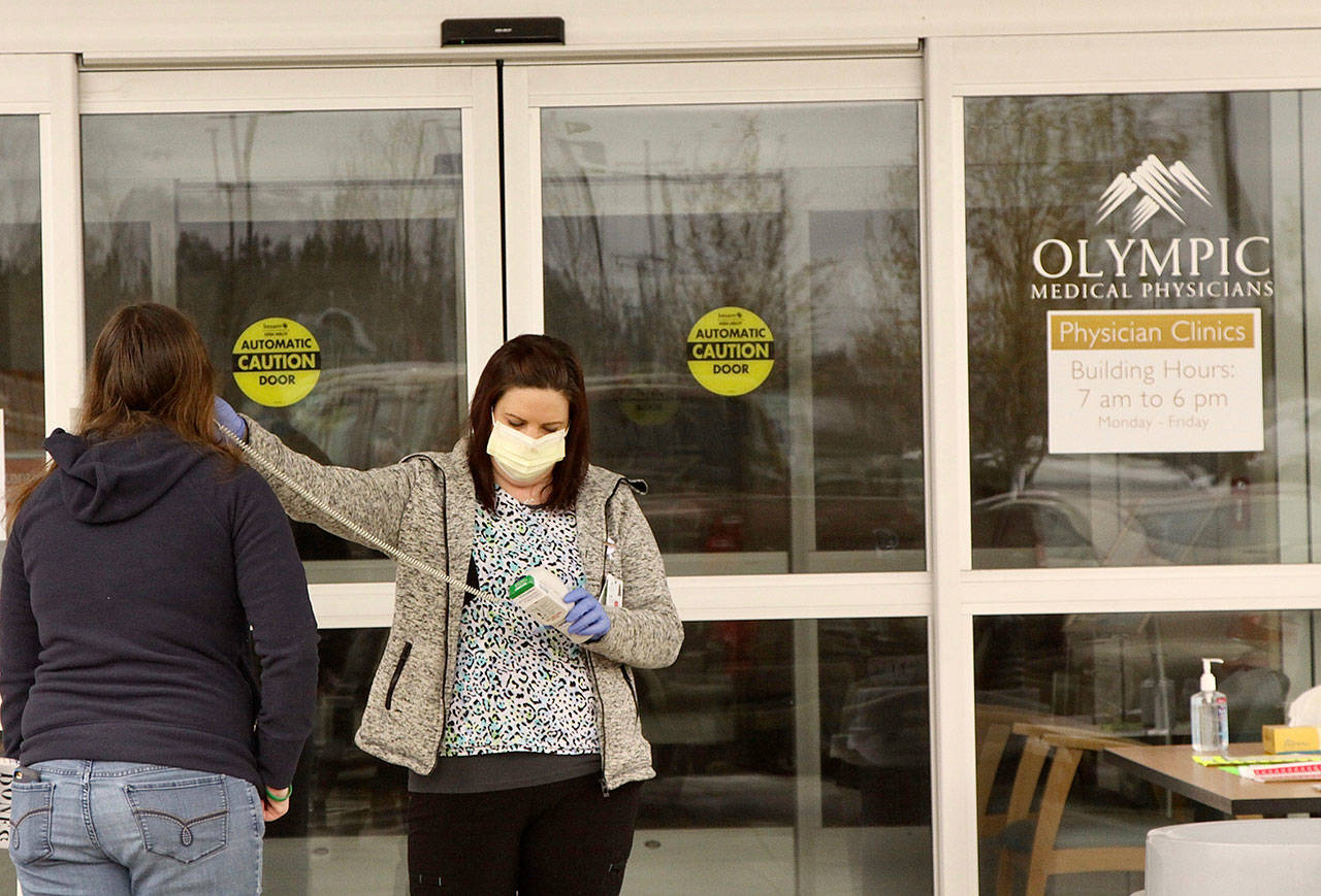 Janine Warren, a medical assistant-apprentice, takes the temperature of a visitor to the Olympic Medical Physicians Clinic at 907 Georgiana St., in Port Angeles. After they are checked for fever, each person is given a visitor/patient tag and asked to use hand sanitizer before entering the clinic. (Dave Logan/For Peninsula Daily News)