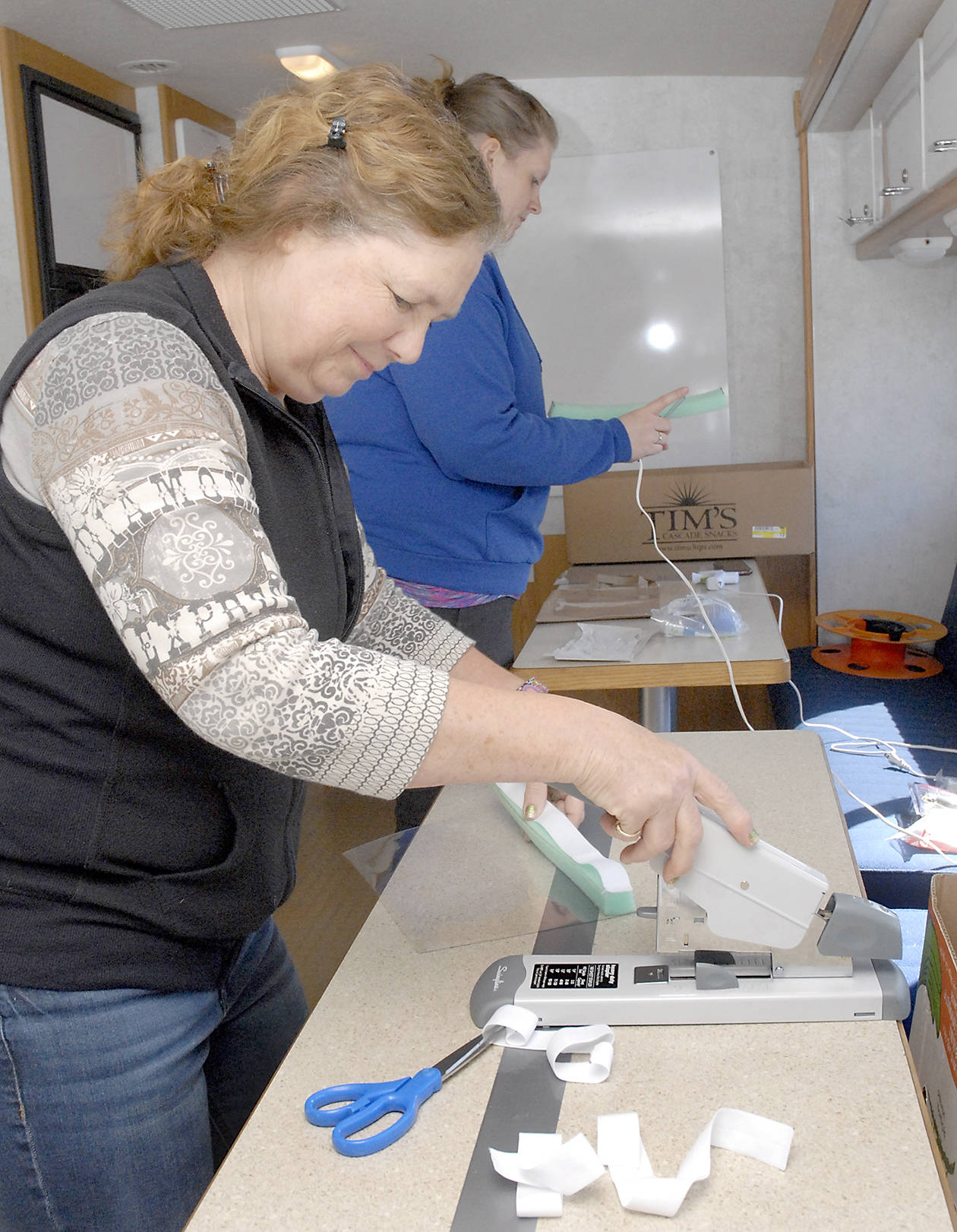 Volunteers Donna Fraser of Port Angeles, front, and Lori Shafer of Joyce fashion homemade face shields to be used by first responders when interacting with potential COVID-19 patients. The pair were working last week in the county’s emergency management vehicle outside the Clallam County Courthouse in Port Angeles. Photo by Keith Thorpe/Olympic Peninsula News Group