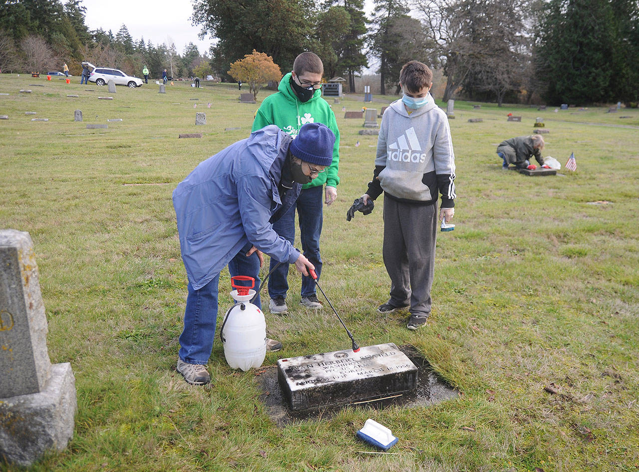 Jan Urfer, secretary with the Michael Trebert Chapter of the Daughter of the American Revolution, works with scouts Hunter Halverson and Cayden Beauregard from Sequim Troop 90 to clean headstones and grave markers at Sequim View Cemetery on Nov 28.