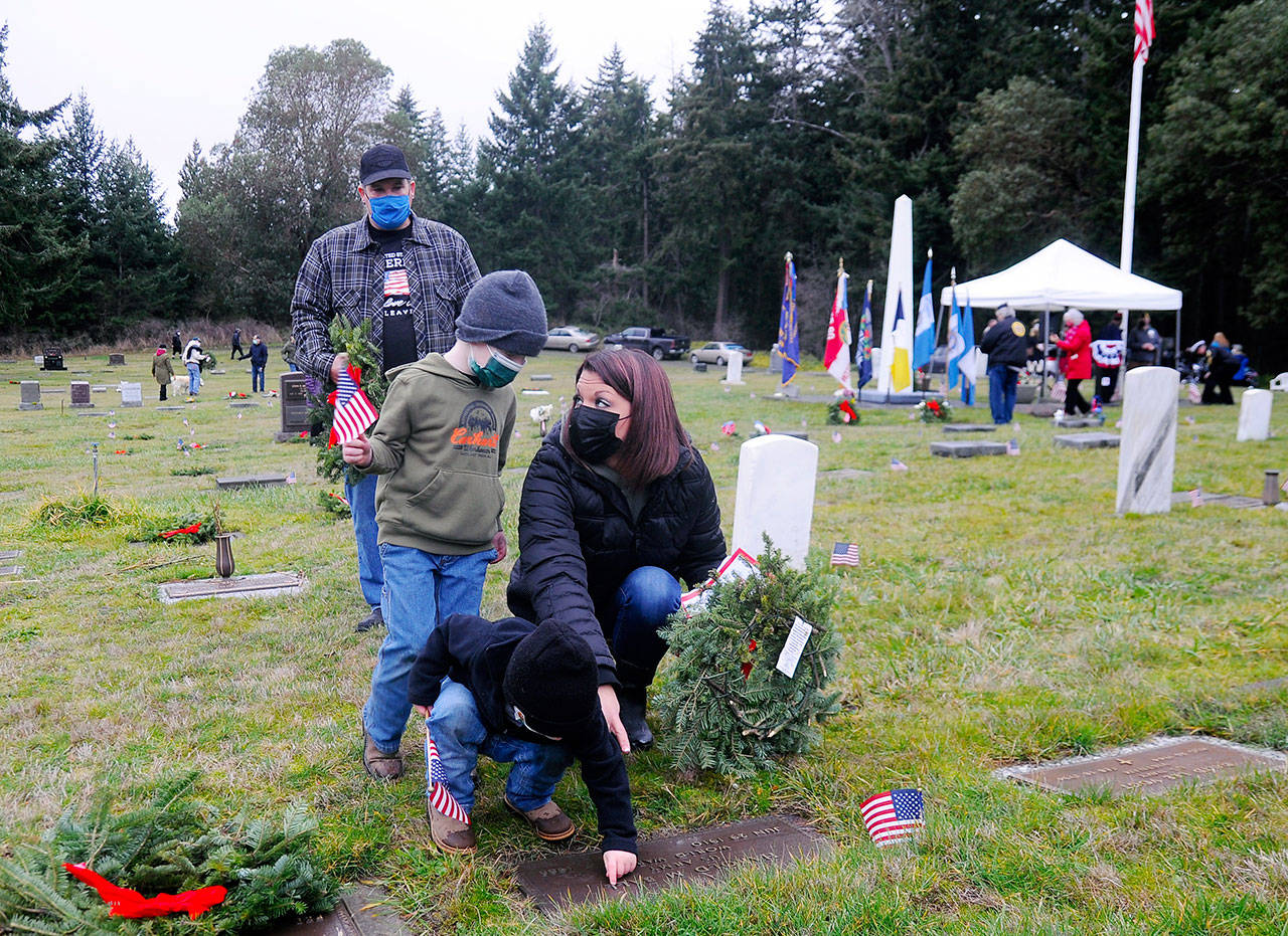 Jennifer Groves of Port Angeles helps sons Blake, 5 (standing), and 2-year-old Bryce, place a wreath on a veteran’s grave marker Saturday, as Groves’ stepfather Bobby Yaun looks on. Groves said she attended the event “to teach my men to show honor.”