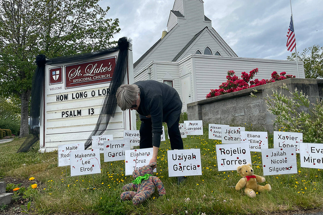 Sequim Gazette photo by Matthew Nash/ Rev. ClayOla Gitane, rector at St. Luke’s Episcopal Church, places signs and bears to remember the victims of the May 24 shooting in Robb Elementary in Uvalde, Texas. More signs were being made inside and later placed to honor the 21 victims.