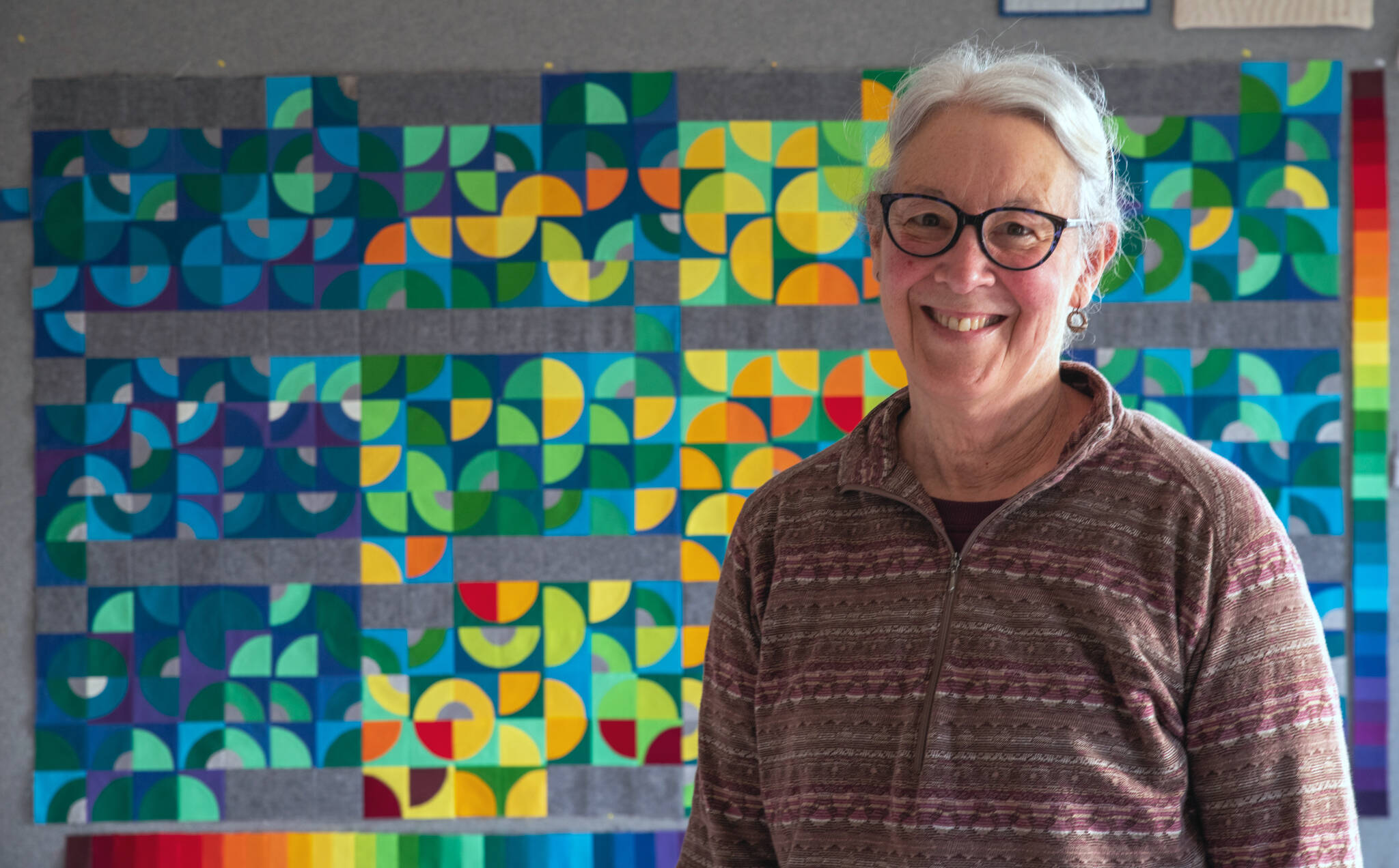 Sequim Gazette photo by Emily Matthiessen / Sequim fiber artist Marla Varner stands in front of her temperature quilt. Each square is color coded to the high and low temperatures of each day of 2021 in her neighborhood in Sequim, with the smallest quarter circles signifying precipitation. This portrait photo earned photographer Emily Matthiessen a third place in the Washington Newspaper Publishers Association’s 2022 Better Newspaper Contest.