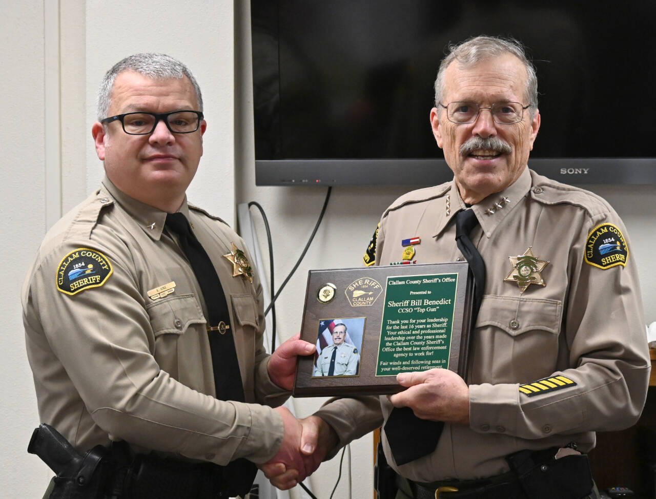 Outgoing Clallam County sheriff Bill Benedict, right, receives a plaque commemorating his years of service from incoming sheriff Brian King at a retirement party in Port Angeles on Dec. 27.