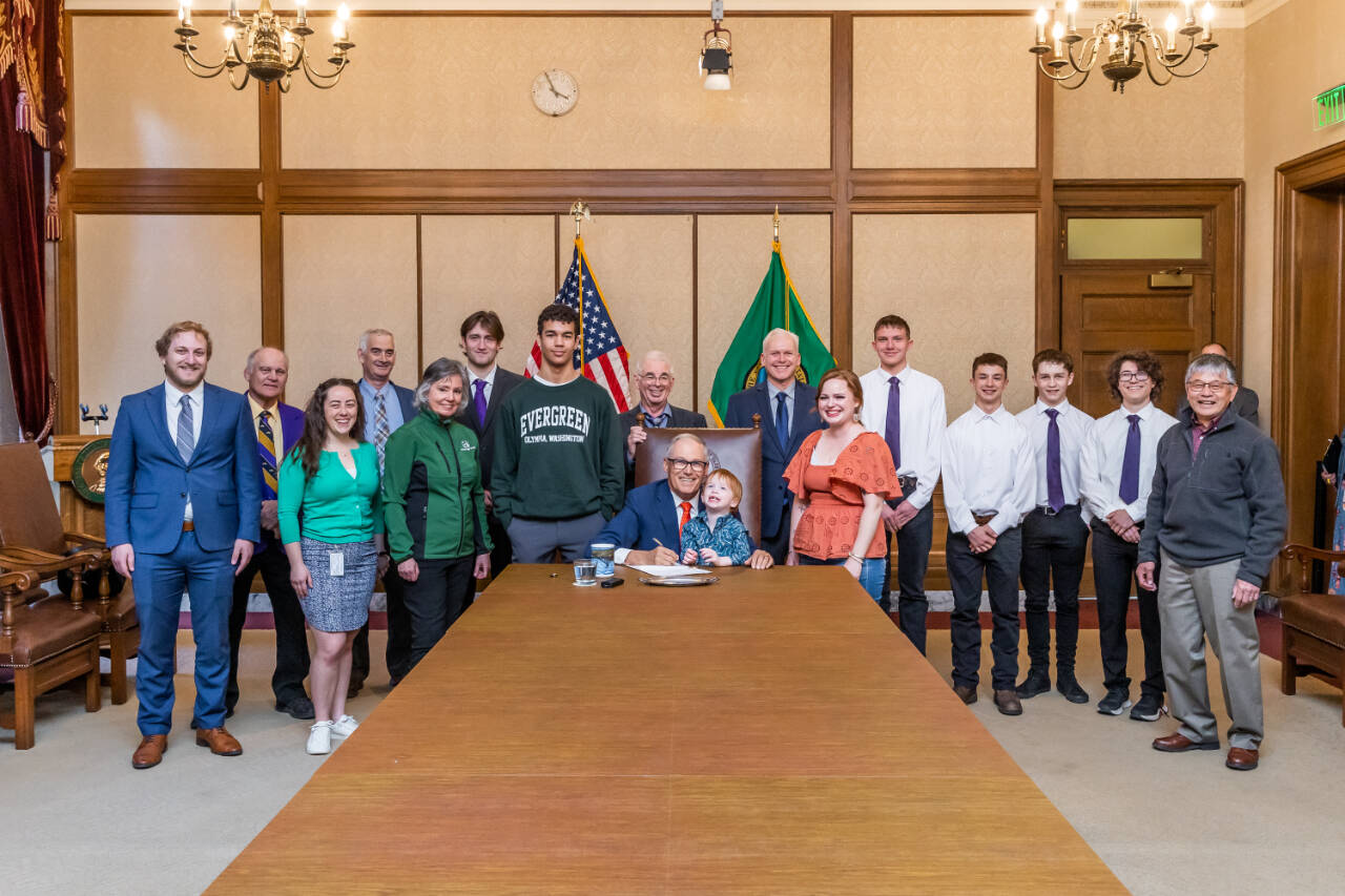 Photo courtesy of Washington State Legislative Support Services / Gov. Jay Inslee, center, signs Substitute Senate Bill No. 5687 on April 25 — legislation called the Charles Cate II Act that bolsters the creation and support of postsecondary wrestling grant programs. Joining Inslee are Cate’s son Charley and wife Renee. Behind Inslee is primary bill sponsor Sen. Kevin Van De Wege and Sequim wrestling advocate Randall Tomaras, along with wresters and wrestling advocates. At far right is SHS wrestling coach Steve Chinn.