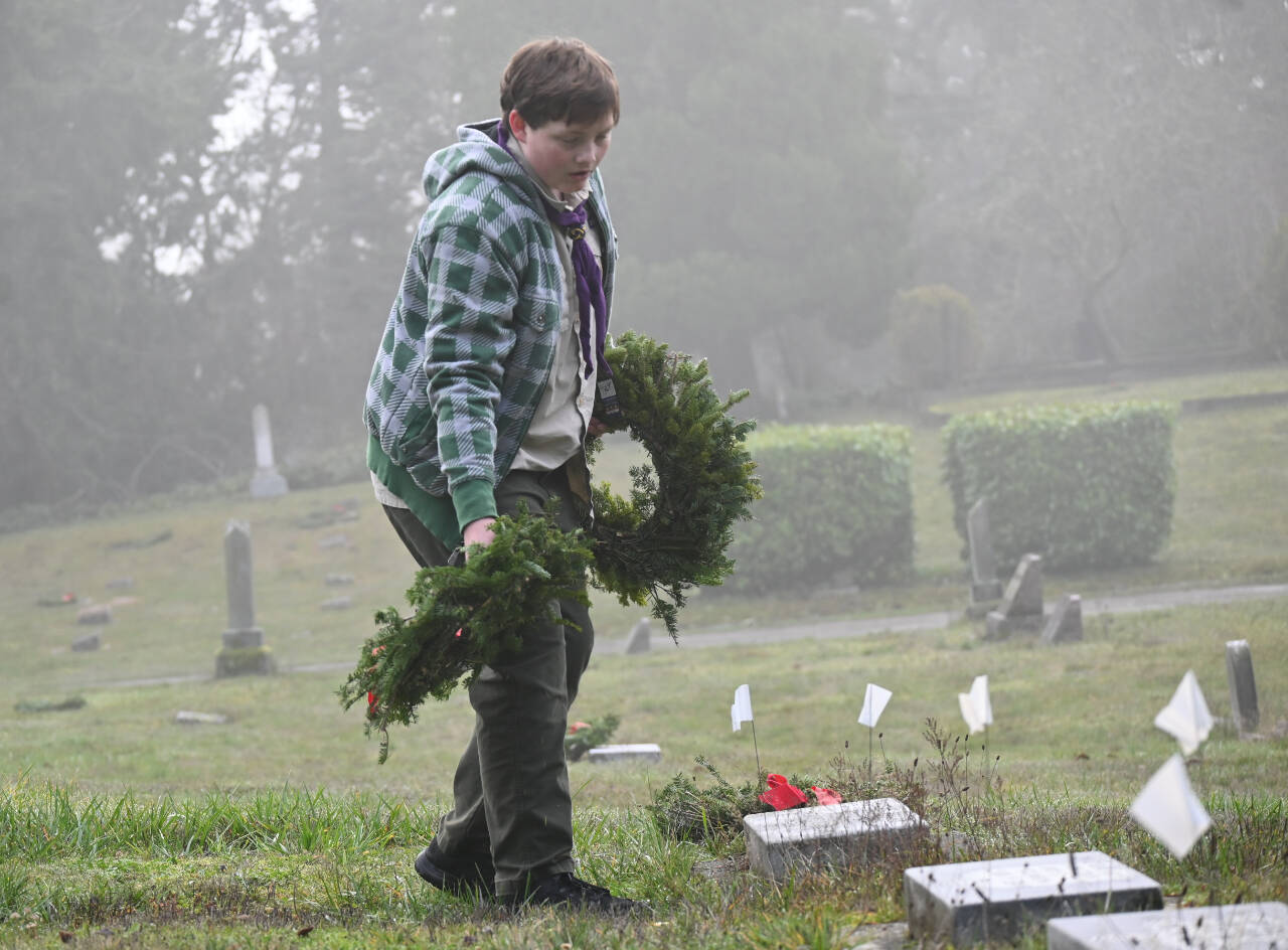 Sequim Gazette photo by Michael Dashiell / Brayden Baritelle and fellow BSA scouts helpplace wreaths on headstones and grave markers at Sequim View Cemetery on Dec. 16.