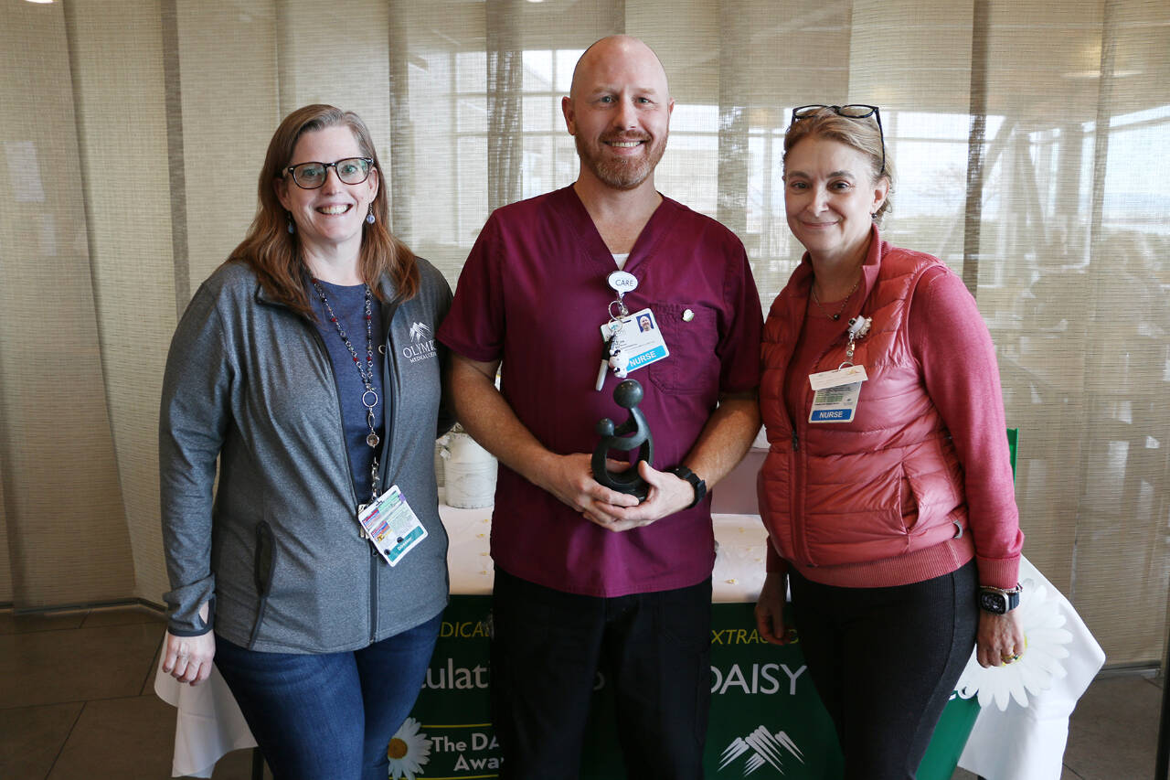 Photo courtesy of Olympic Medical Center / Registered nurse Casey Peterson accepts his DAISY Award for Extraordinary Nurses from Denise Harman, director of medical/surgical/pediatrics, left, and and Chief Nursing Officer Vickie Swanson.
