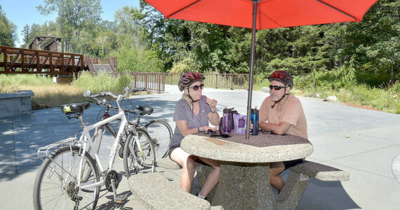 Twyla and Doug Falsteisek, who split their time between Port Angeles and Sun City West, Ariz., take a break from their bike ride on the patio of the Dungeness River Nature Center along the Dungeness River in Sequim on Wednesday. The couple took advantage of summer weather for an excursion on the Olympic Discovery Trail. (Keith Thorpe/Peninsula Daily News)