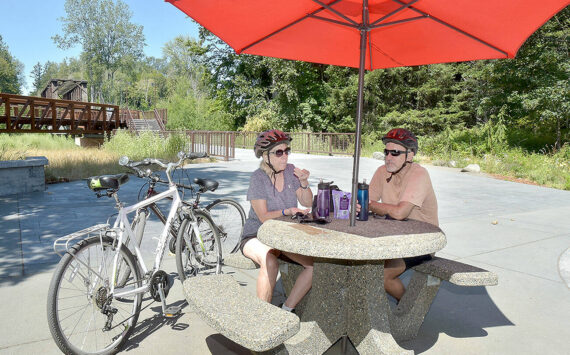 Twyla and Doug Falsteisek, who split their time between Port Angeles and Sun City West, Ariz., take a break from their bike ride on the patio of the Dungeness River Nature Center along the Dungeness River in Sequim on Wednesday. The couple took advantage of summer weather for an excursion on the Olympic Discovery Trail. (Keith Thorpe/Peninsula Daily News)