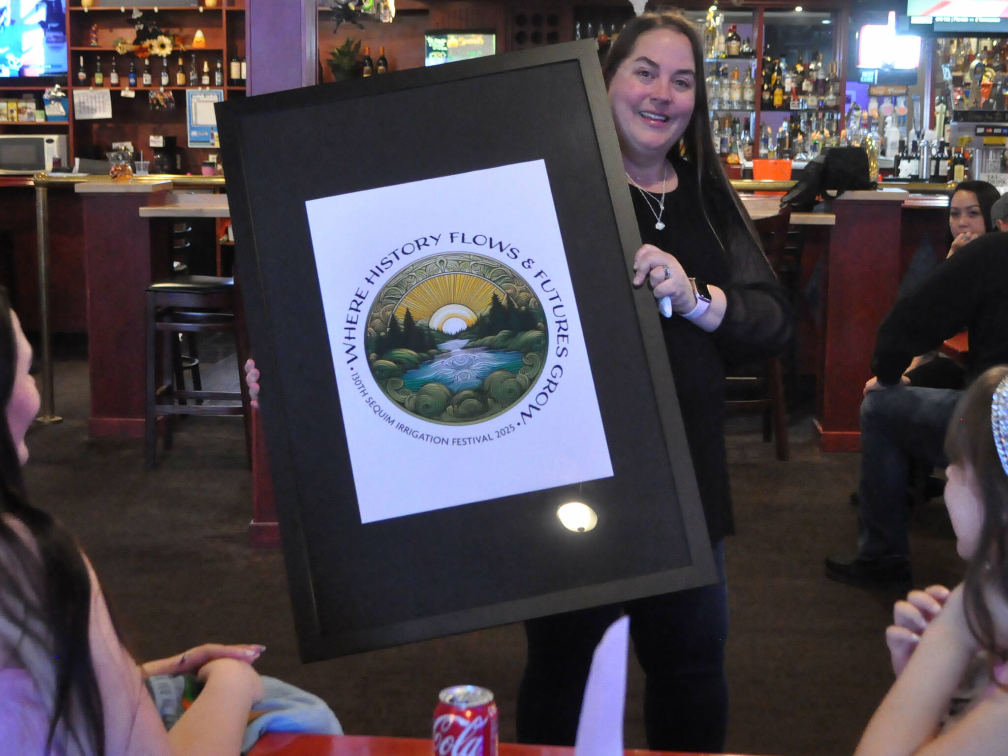 Sequim Gazette photo by Matthew Nash
Michelle Rhodes, executive director of the Sequim Irrigation Festival, shows festival royalty the new logo and tagline “When History Flows and Futures Grow” for the 130th festival on Oct. 12 at the Oasis Bar and Grill. Sherry Scharschmidt designed the logo for the second year.