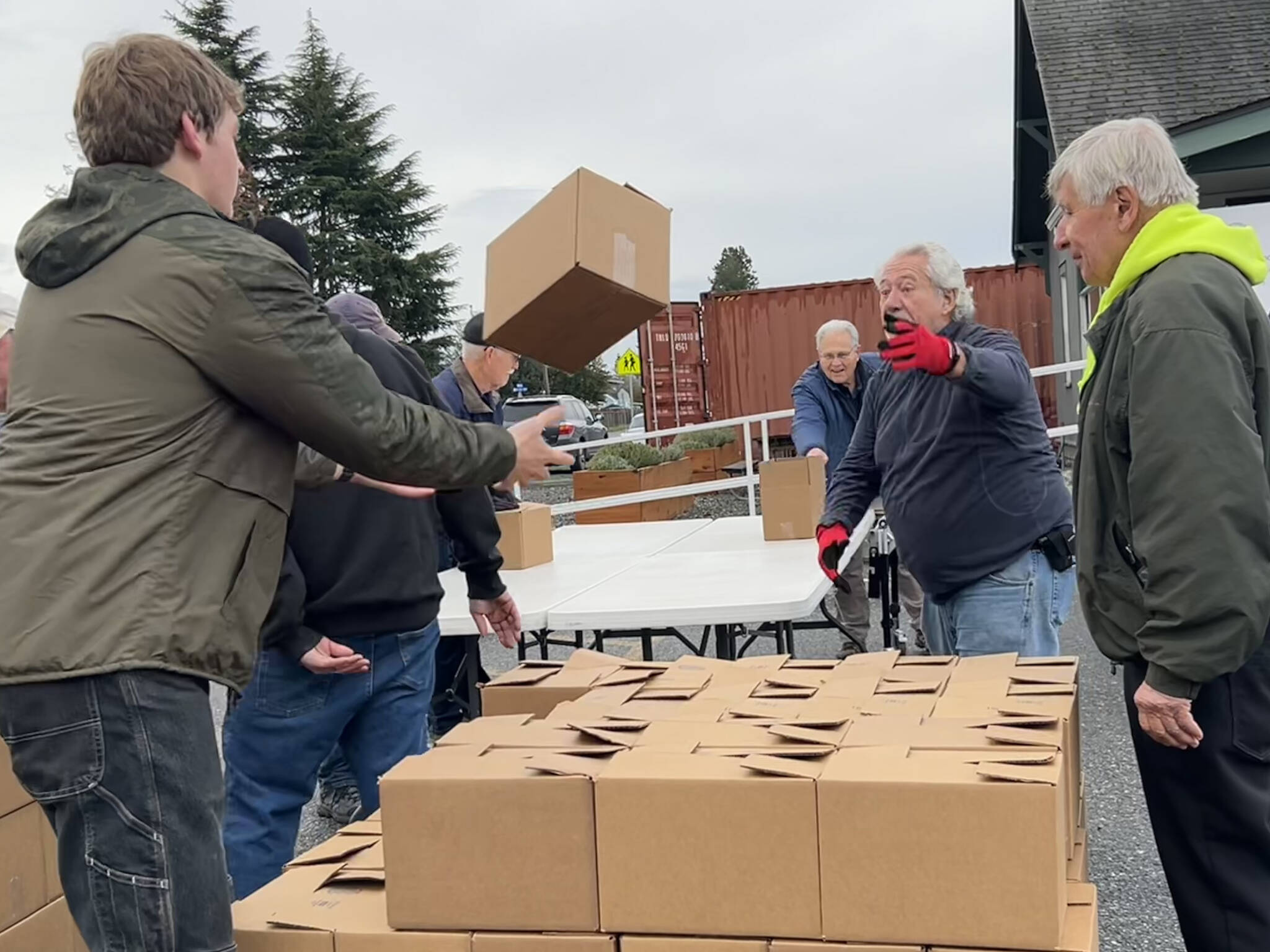 Sequim Gazette photo by Matthew Nash
Harvey Hochstetter tosses a box of food to Cameron Needham to stack on Nov. 21 with fellow volunteers like Bill Needham, on right, for the Sequim Food Bank’s Holiday Meal Bag Distribution event. Cameron, his father Ty and grandfather Bill were three generations helping the program.