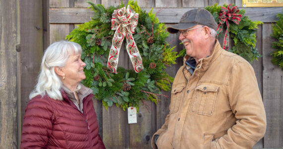 Sequim Gazette photo by Emily Matthiessen
Outside the Christmas Barn at Lazy J Tree Farm, Ann and Steve Johnson smile at each other in front of wreaths Ann prepares with two other women for the Christmas season. Ann says they sell about 70 a year.