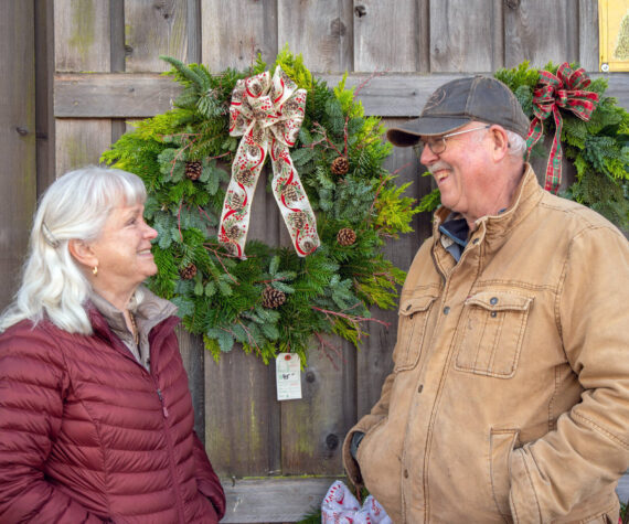 <p>Sequim Gazette photo by Emily Matthiessen</p>
                                <p>Outside the Christmas Barn at Lazy J Tree Farm, Ann and Steve Johnson smile at each other in front of wreaths Ann prepares with two other women for the Christmas season. Ann says they sell about 70 a year.</p>